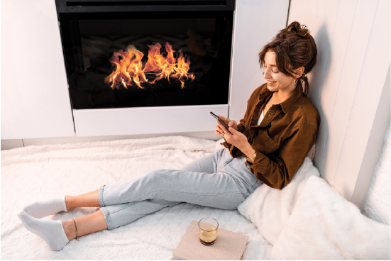 a girl sitting beside a fire place and holding a phone